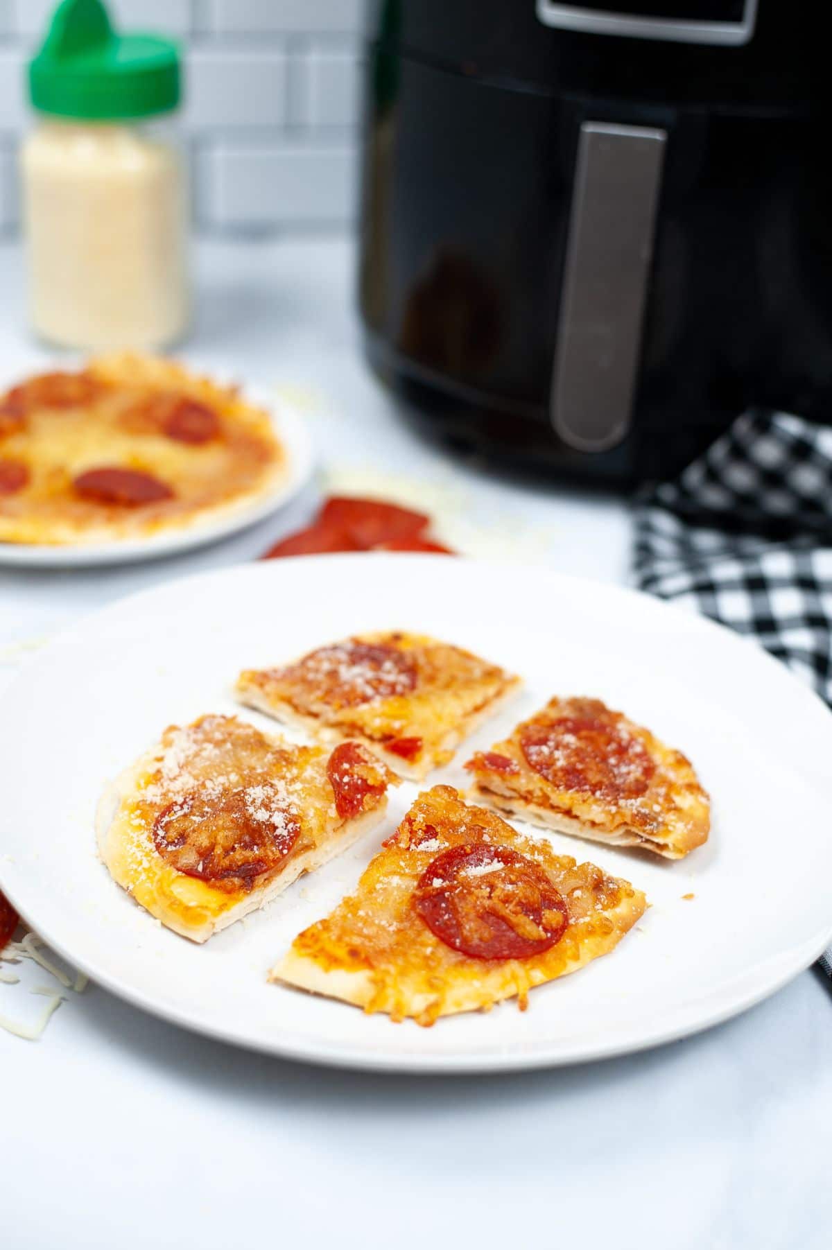 Air Fryer Naan Bread Pizza sliced into 4 pieces on a white plate with an air fryer in the background and another pizza on a plate unsliced.
