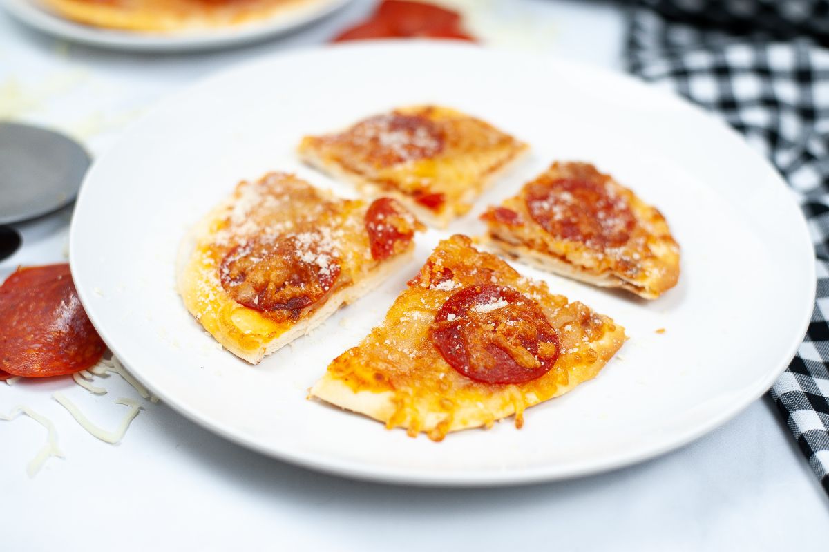 A horizontal shot of an Air Fryer Naan Bread Pizza, sliced into 4 pieces, on a white serving plate.