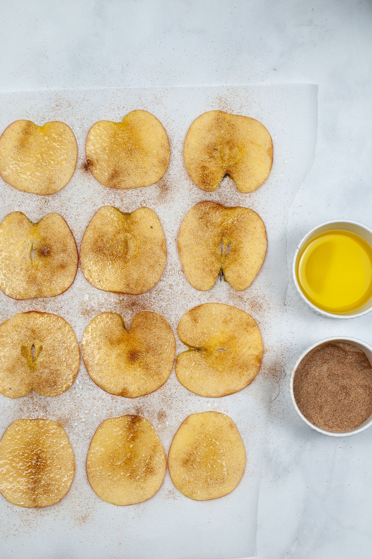 Thin slices of an apple on a parchment paper sprinkled with Cinnamon sugar.