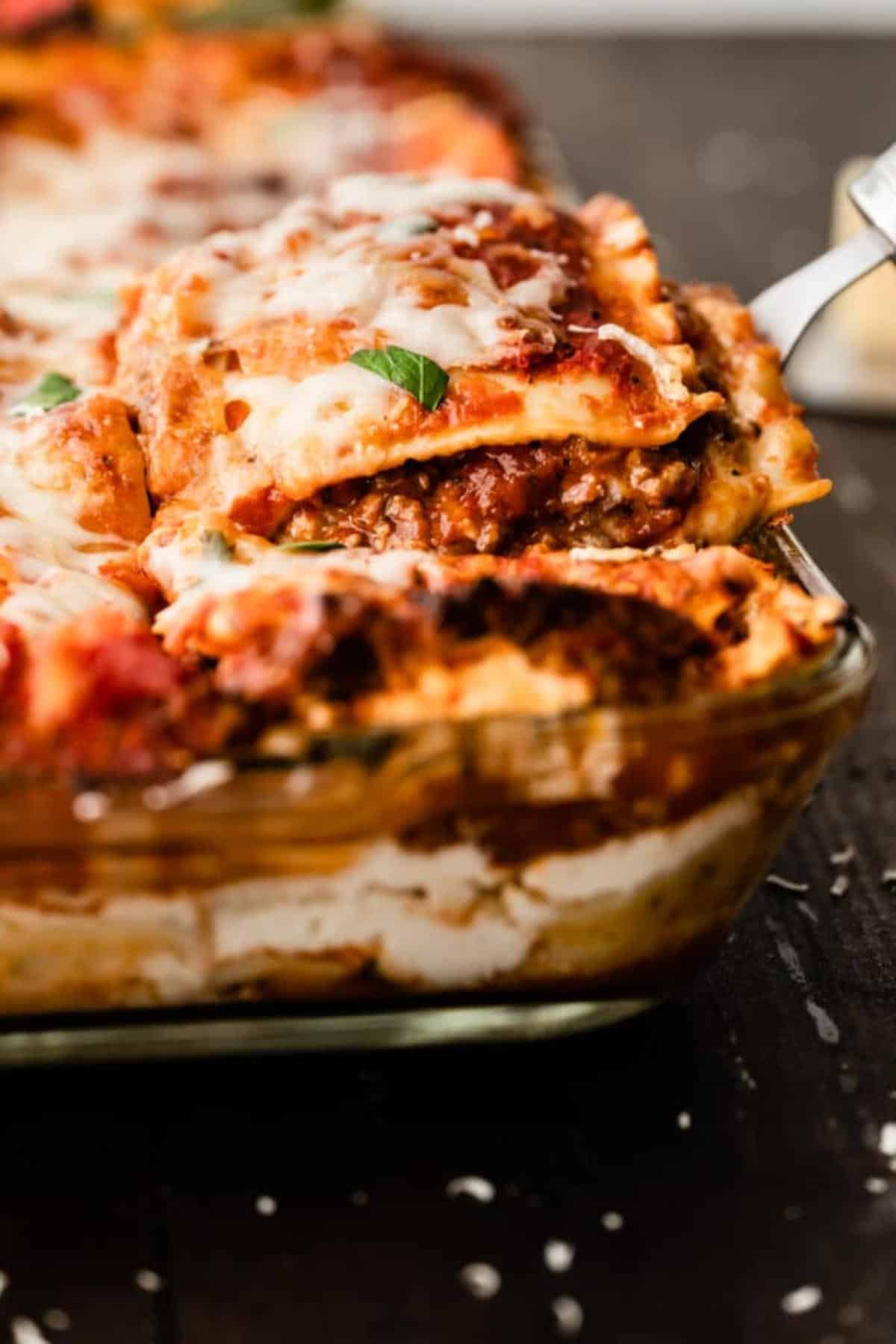 A lasagna being taken out of a baking dish.