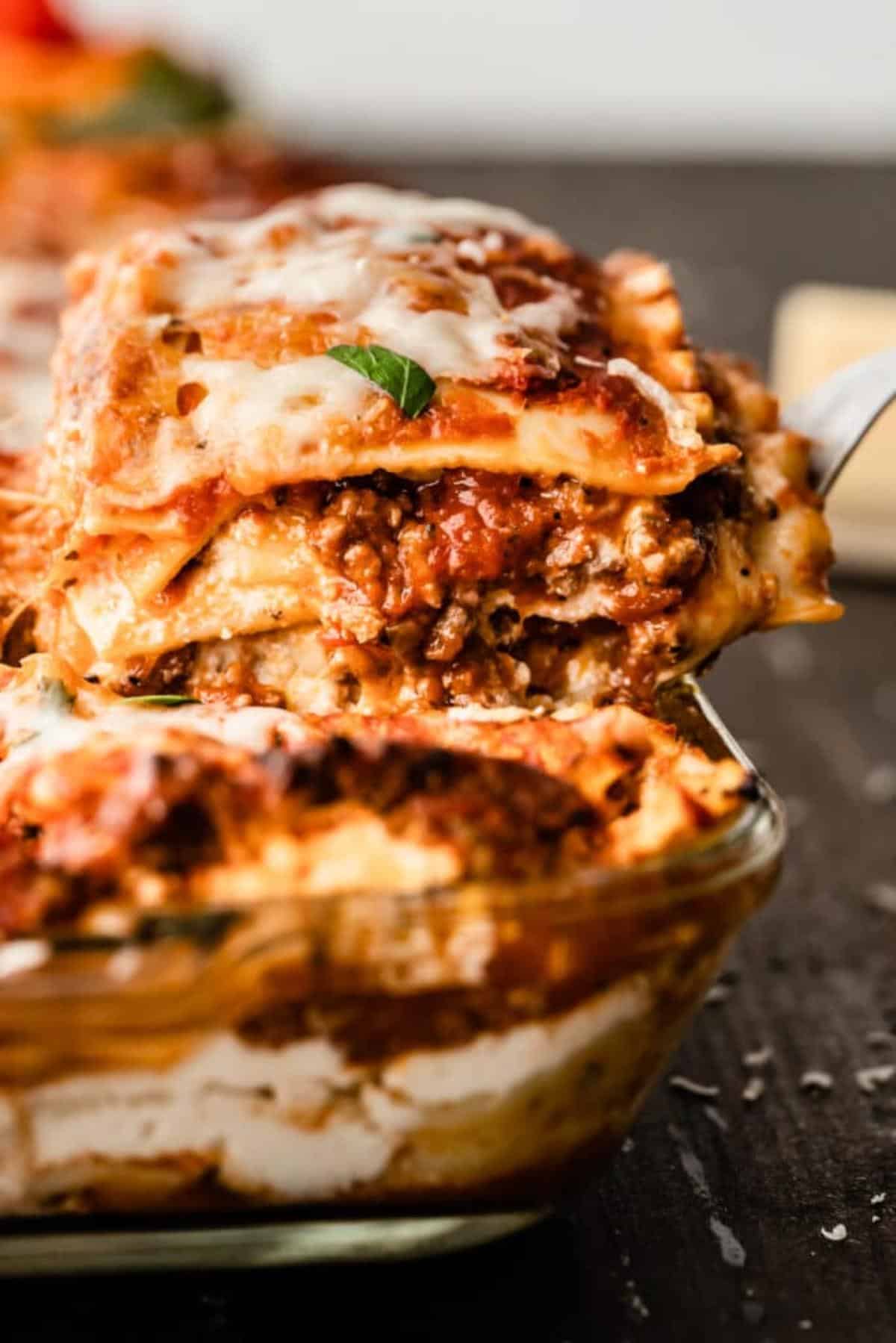 A lasagna being taken out of a baking dish.