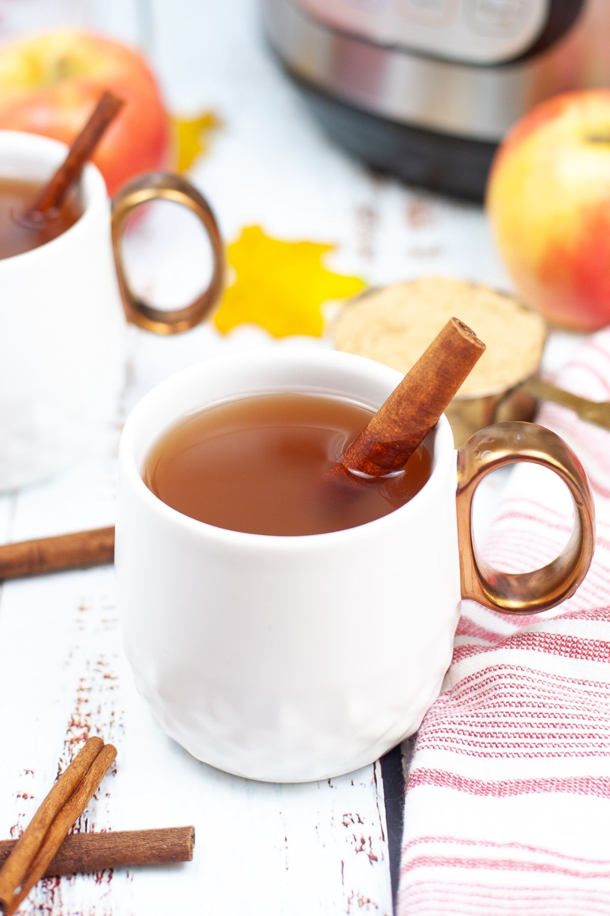 A vertical image of Instant Pot Apple Cider in a white mug with a submerged cinnamon bark.