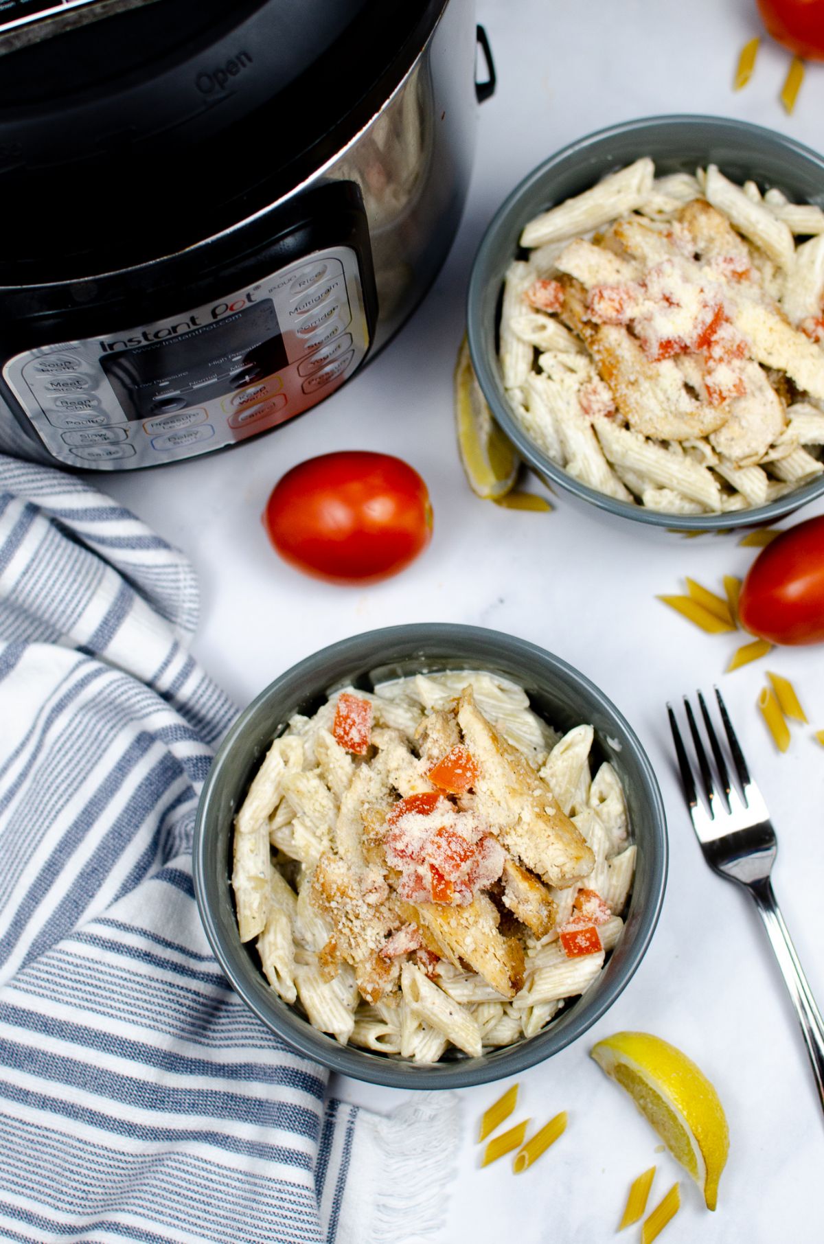 A vertical overhead shot of Instant Pot Cajun Chicken Pasta in a bowl placed at the center and another bowl, the Instant Pot, some tomatoes, and fork around the center bowl.