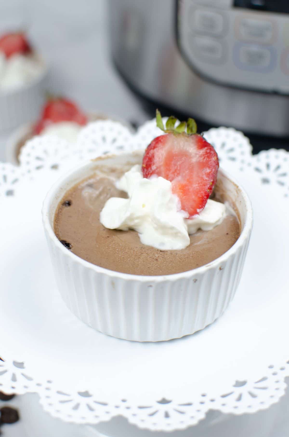A vertical image of Instant Pot Chocolate Mousse in a white ramekin placed at the center of a white circular cake stand.