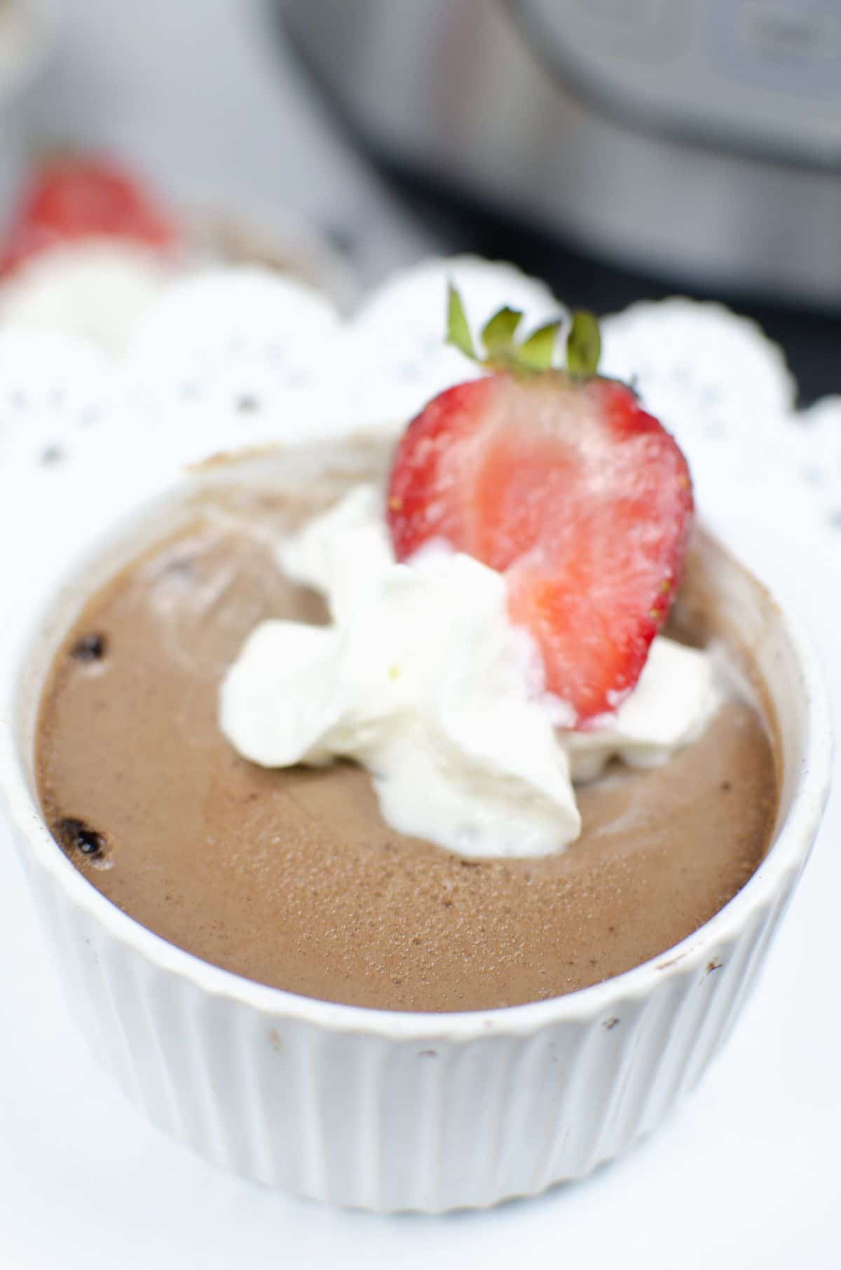 A vertical close up shot of Instant Pot Chocolate Mousse in a white ramekin topped with cream and a slice of strawberry.