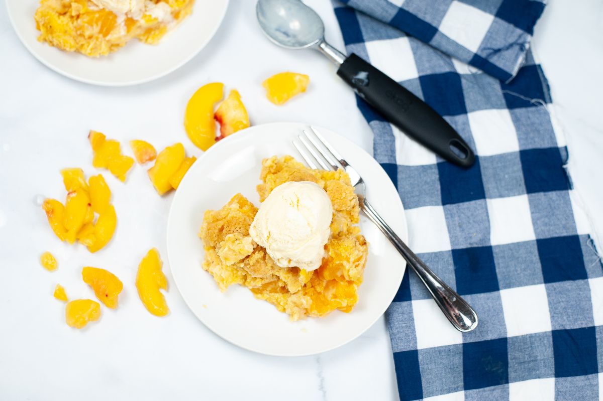 A horizontal overhead shot of Instant Pot Peach Cobbler on a white serving plate, topped with a scoop of ice cream, with a fork beside the peach cobbler