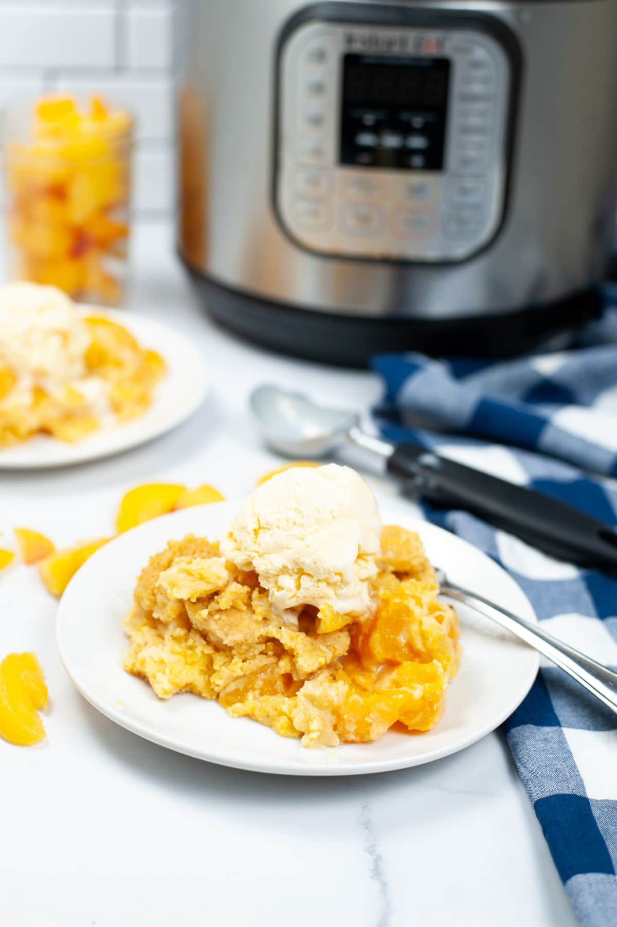 A vertical image of Instant Pot Peach Cobbler on a white serving plate and topped with a scoop of ice cream.