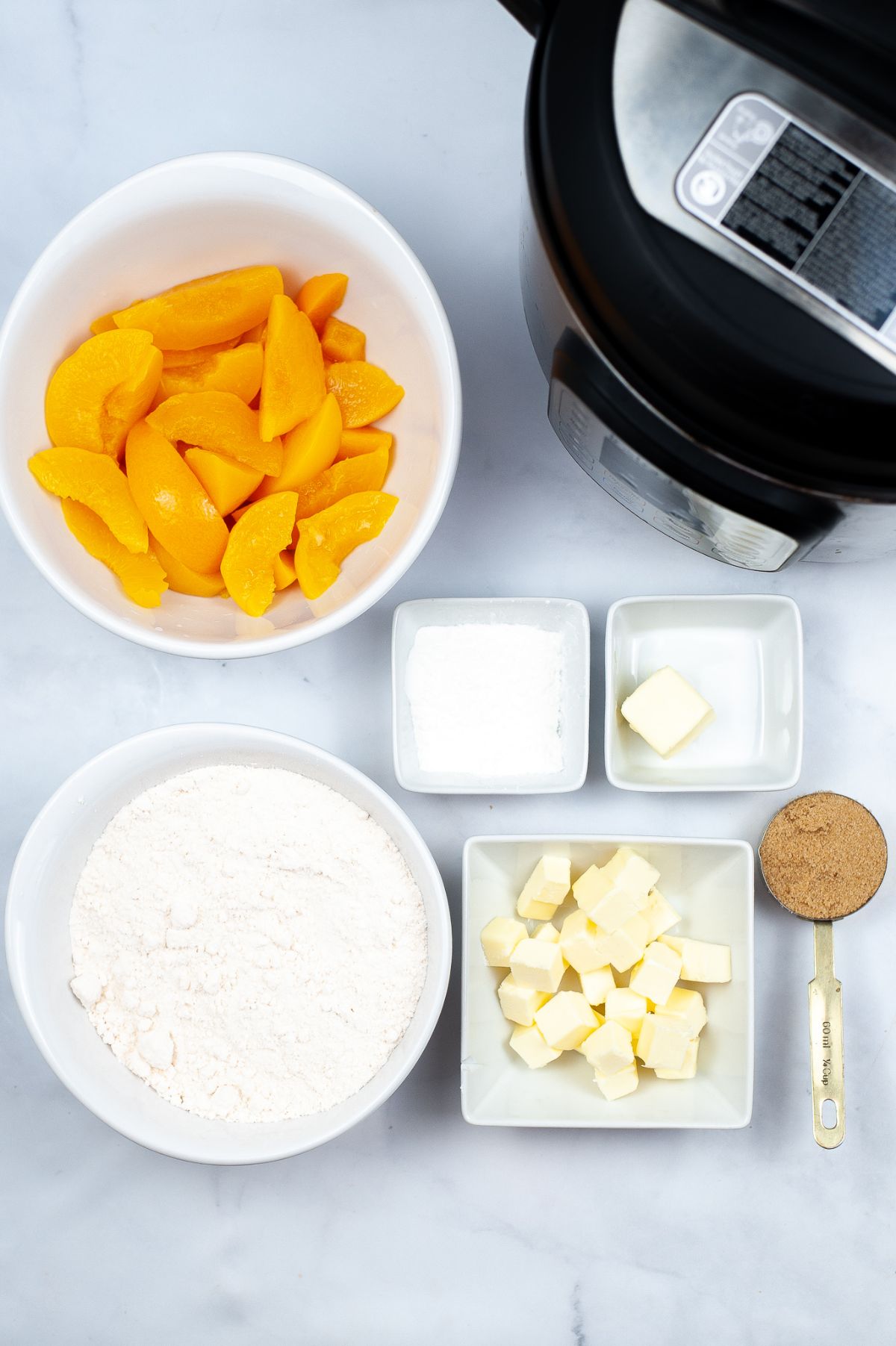 An image of ingredients used to make Instant Pot Peach Cobbler: peaches, cake mix, butter, brown sugar, and cornstarch.