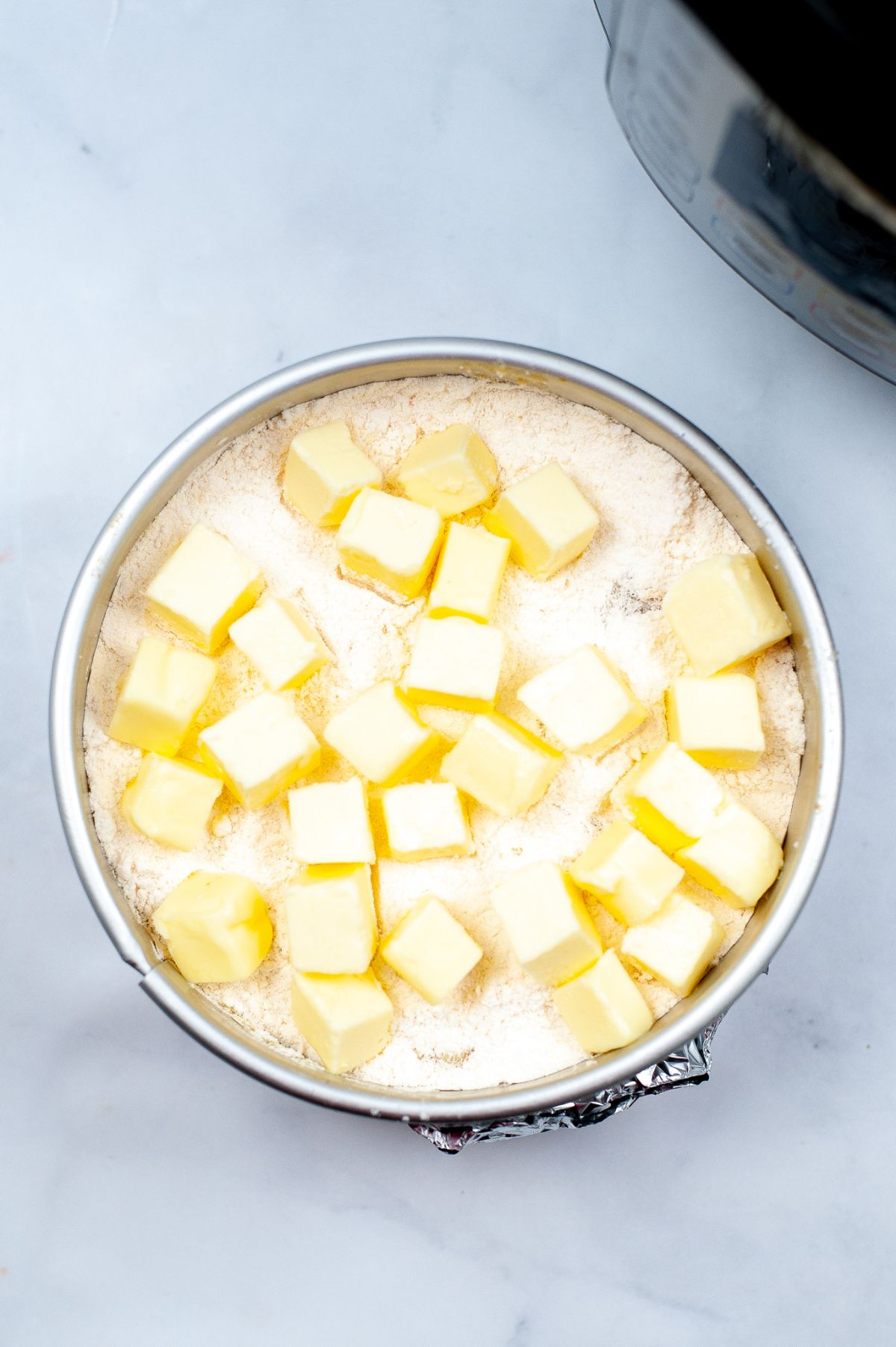 A circular baking pan with the peach and cake mixture topped with cornstarch and cubed butter.
