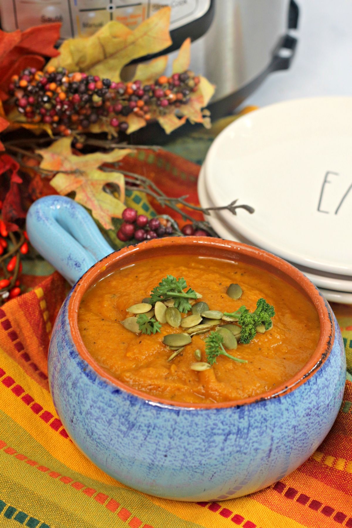 A vertical image of Instant Pot Pumkin Soup in a blue ceramic bowl with orange interior that matches the soup.