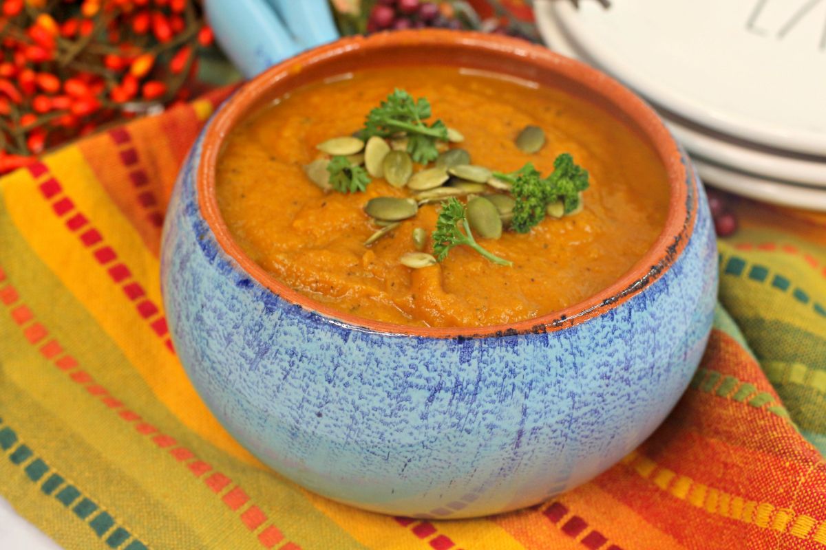 A horizontal image of Instant Pot Pumpkin Soup in a blue ceramic bowl with orange interior and highlights the soup toppings  pumpkin seeds and parsley.
