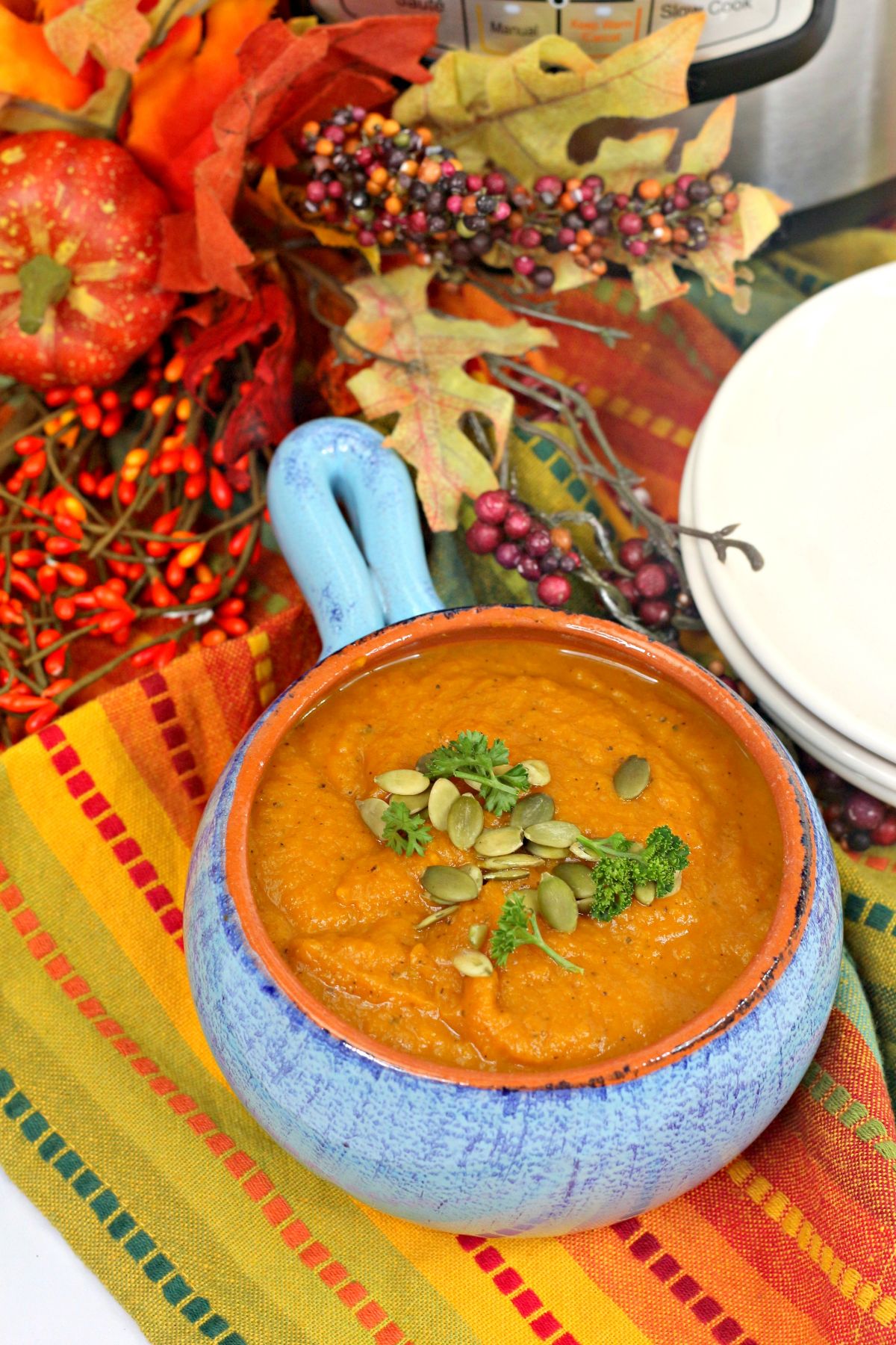 A vertical image of Instant Pot Pumpkin Soup in a blue ceramic bowl with orange interior and highlights the soup toppings pumpkin seeds and parsley.