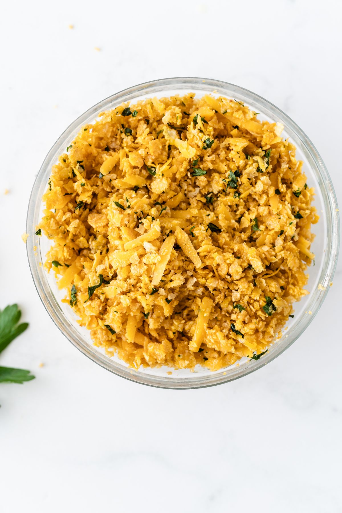 A bowl with combined cornflakes, cheddar cheese and parsley to make the topping.