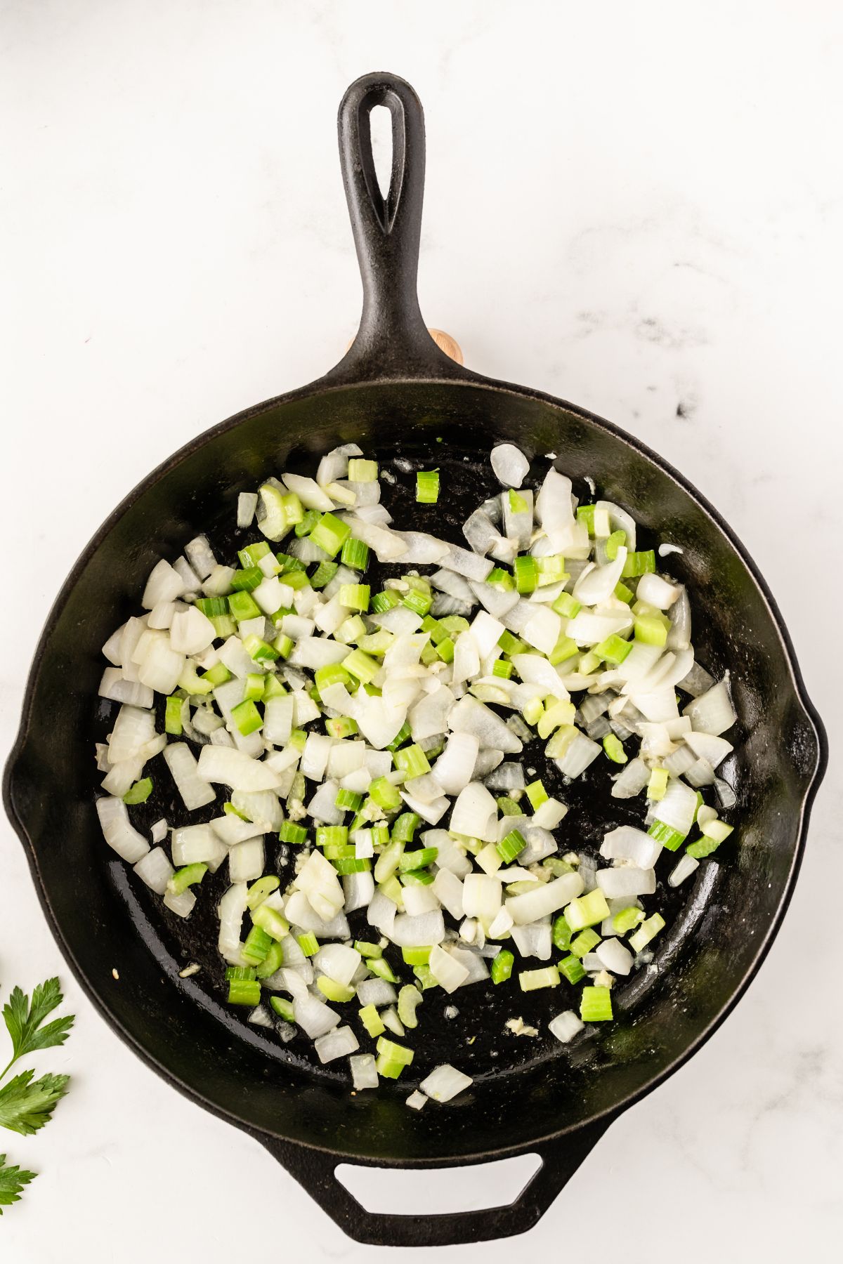 An iron skillet with chopped onion and celery being cooked.