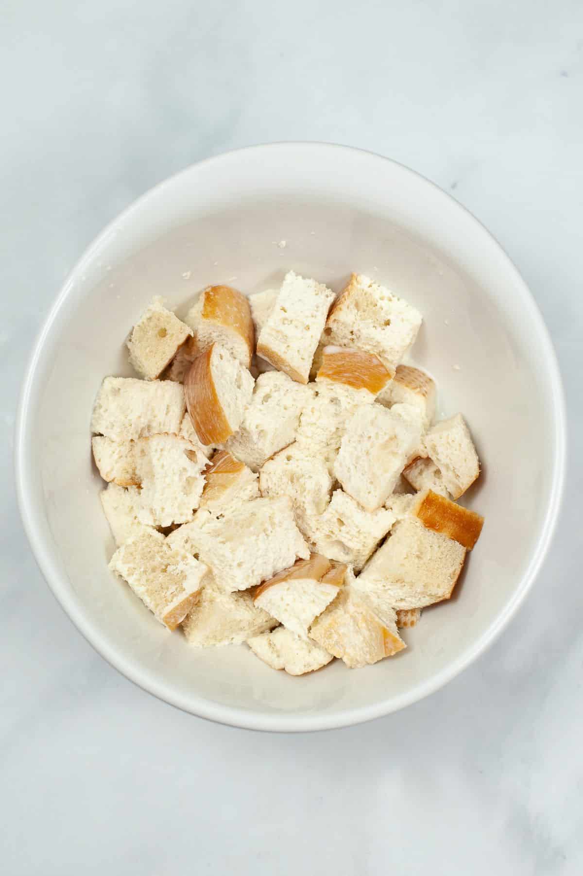 bread cubes, heavy whipping cream and milk are being combined in a bowl.