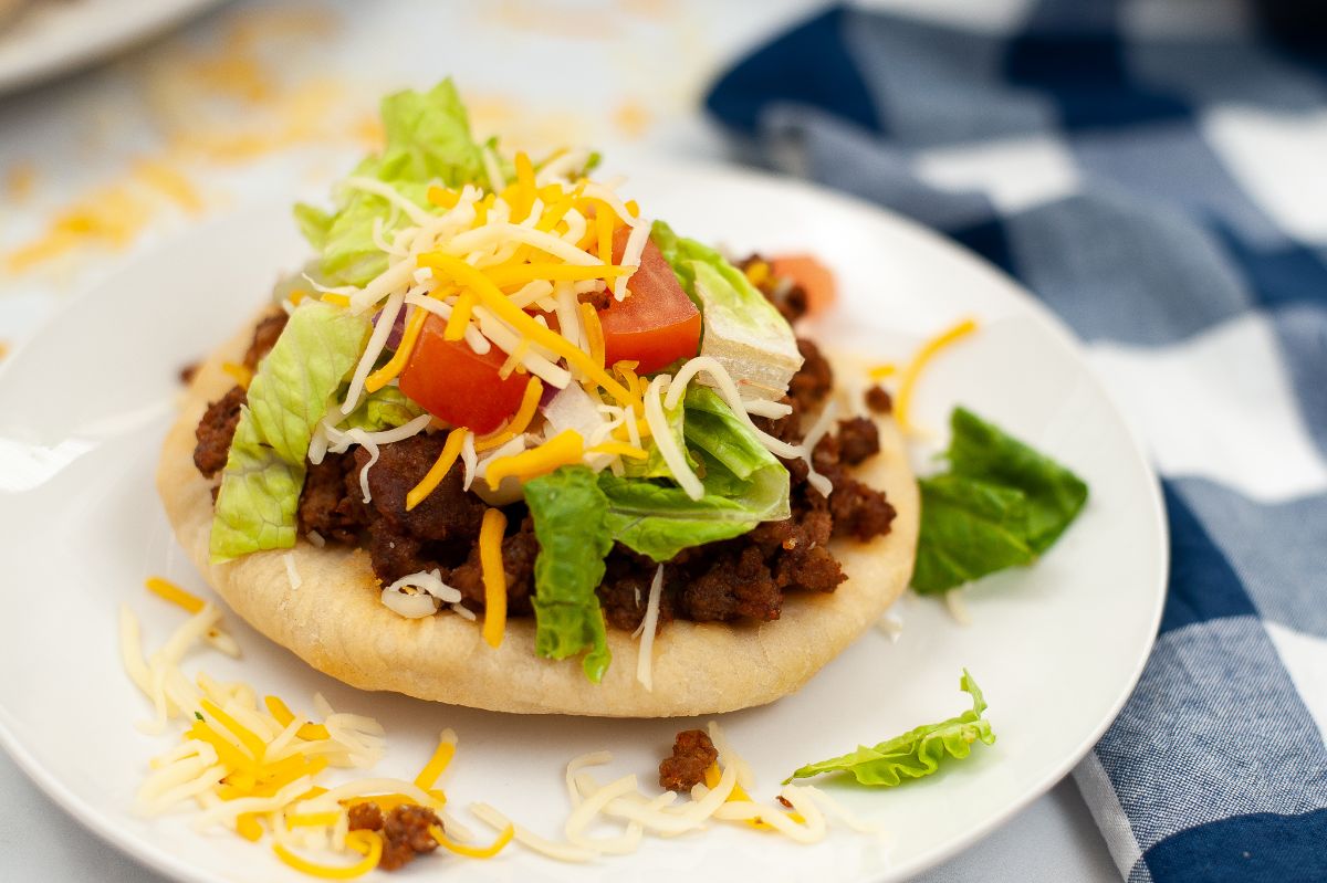 A horizontal image of Air Fryer Indian Bread Tacos highlighting the generous amount of taco meat, lettuce, cheese, onion, and tomatoes.