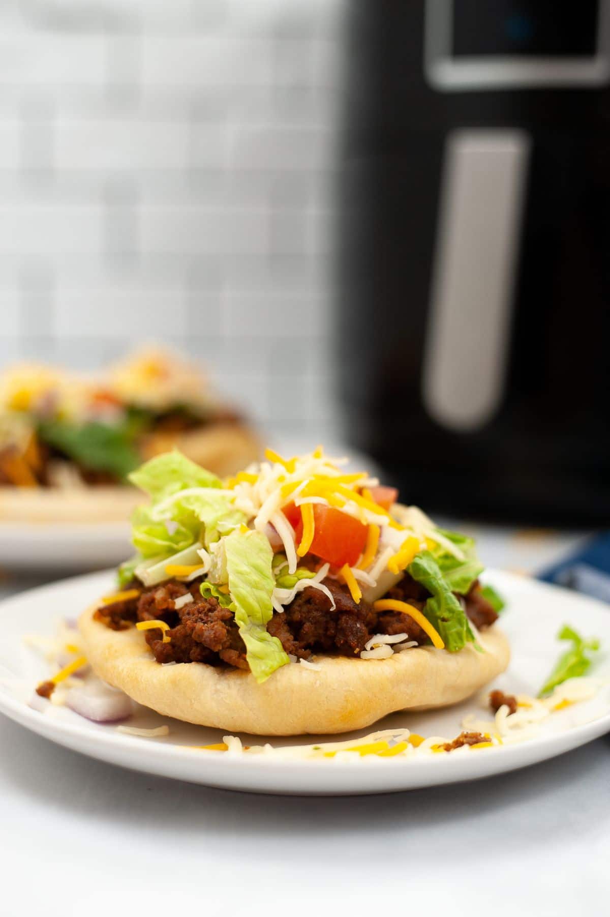 A view from the side of the Air Fryer Indian Bread Tacos, shot vertically with the air fryer and other taco bread blurred behind it.