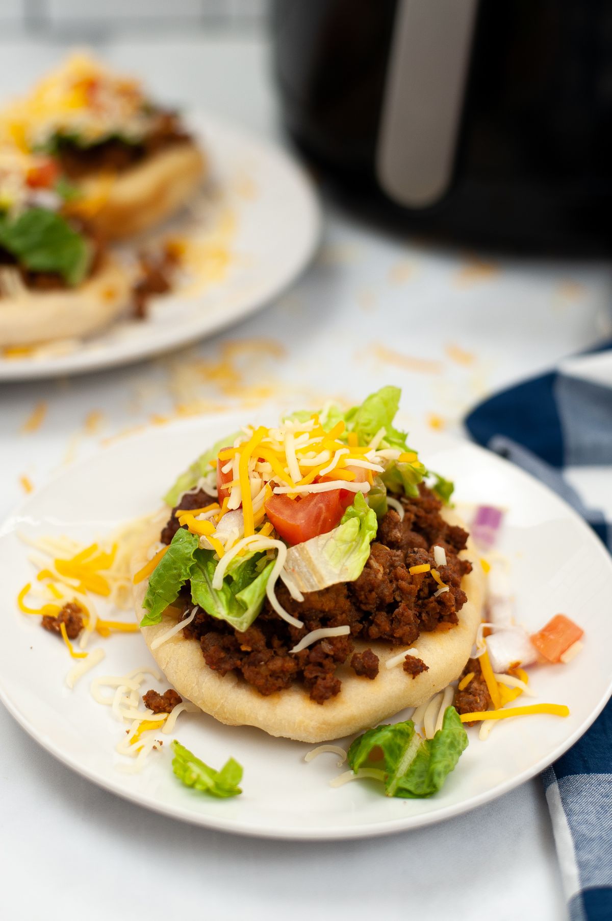 A vertical image of Air Fryer Indian Bread Tacos on a white plate with a generous amount of taco meat and other taco ingredients on top of it. 
