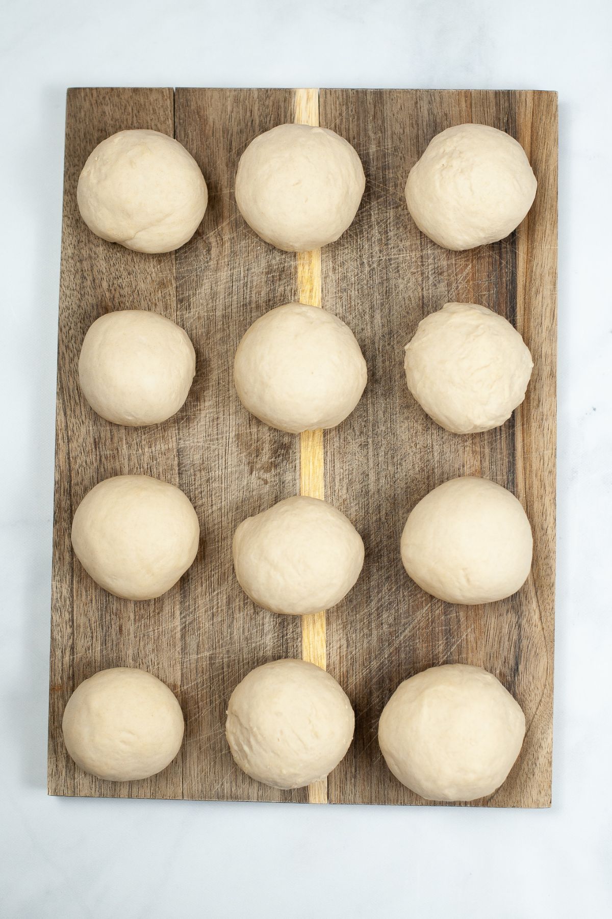 12 shaped dough balls as big as golf balls placed on top of a wooden chopping board.
