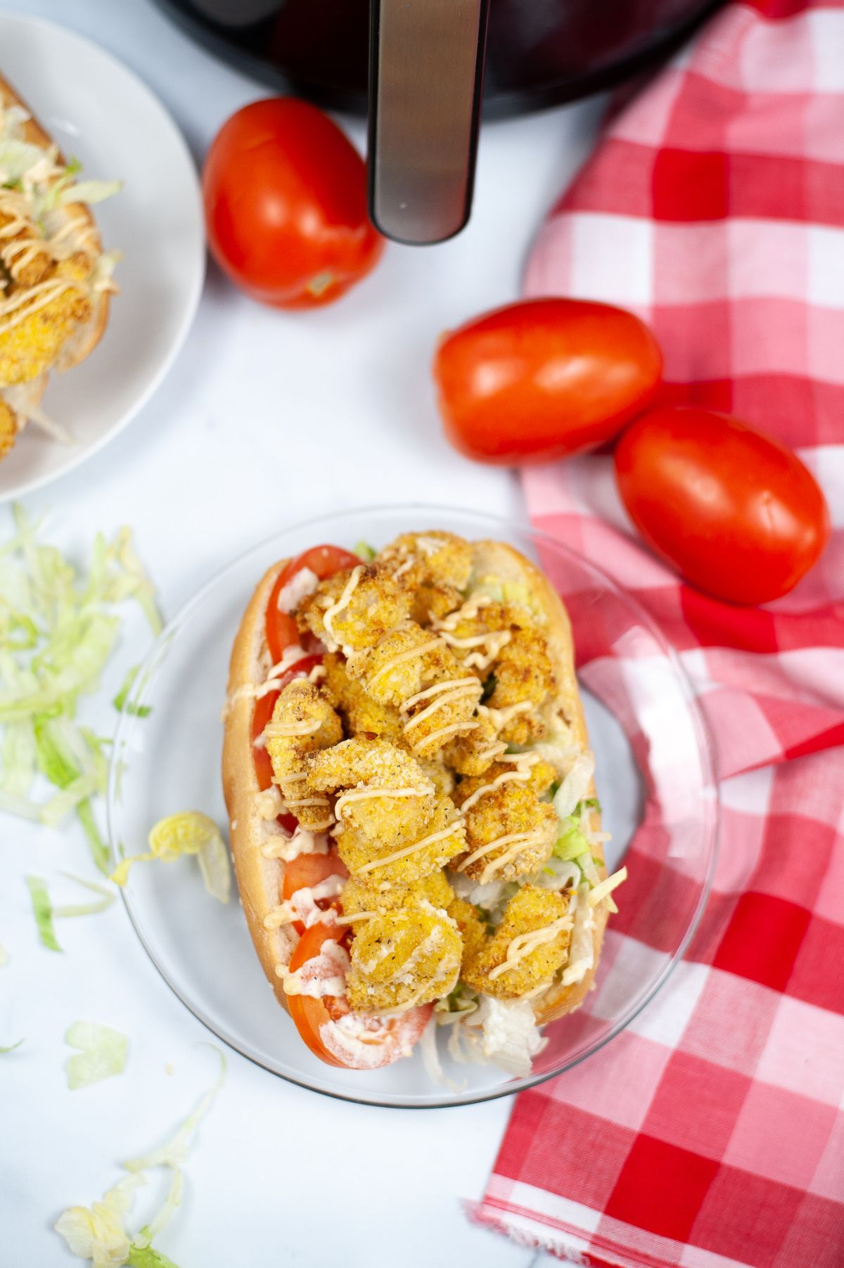 Overhead vertical image of Air Fryer Shrimp Po Boy on a glass serving plate with tomatoes on the side.