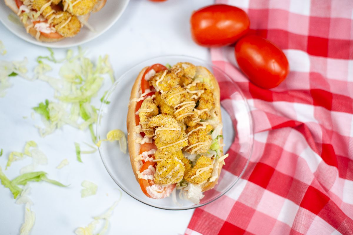 Overhead horizontal image of Air Fryer Shrimp Po Boy on a glass serving plate with tomatoes on the side.
