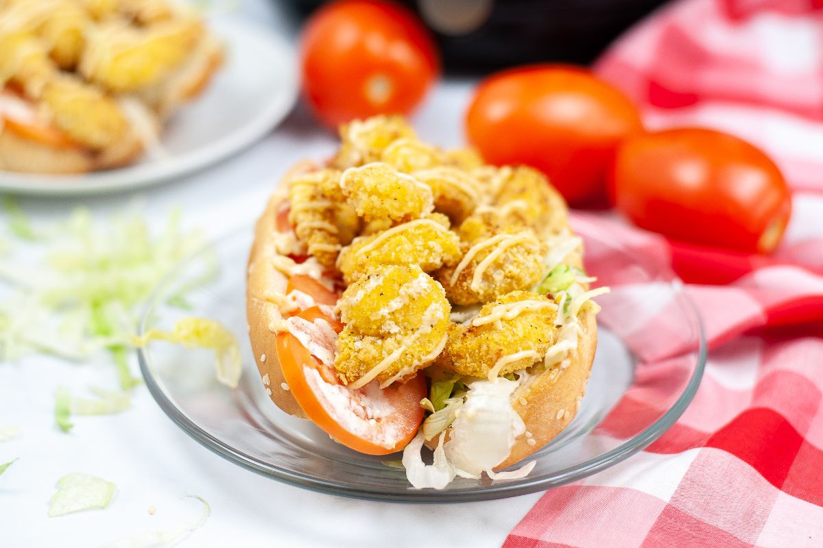 Horizontal image of Air Fryer Shrimp Po Boy on a glass serving plate with tomatoes on the side.