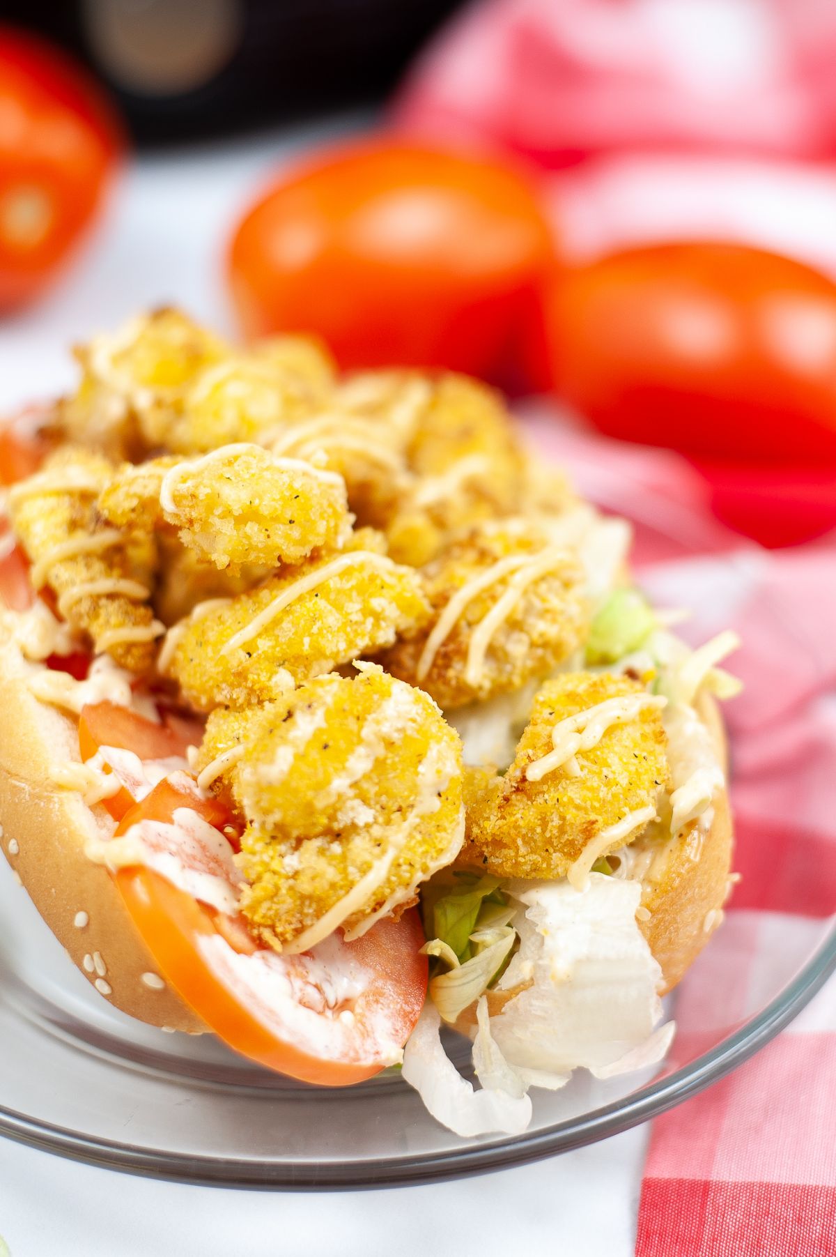 Vertical image of Air Fryer Shrimp Po Boy on a glass serving plate with blurred tomatoes in the background.
