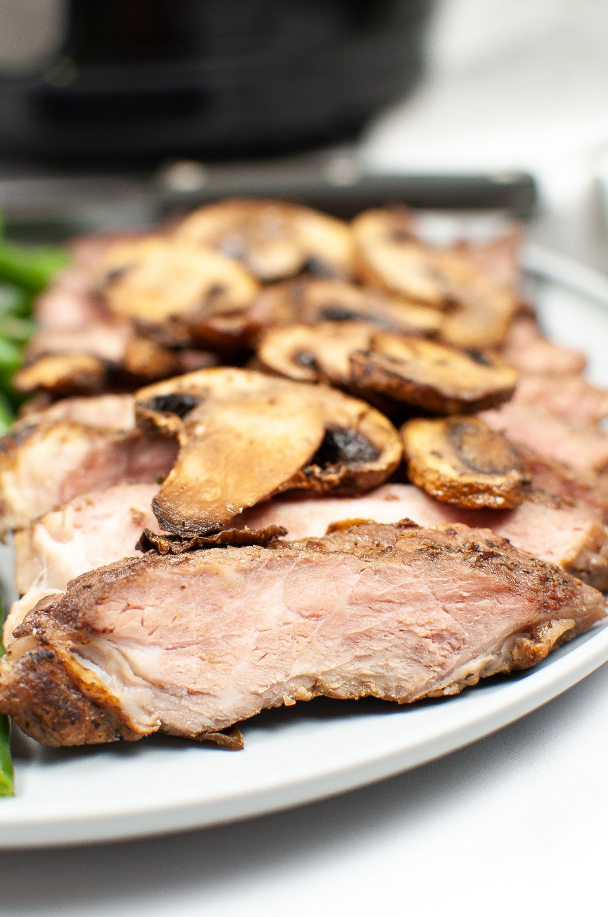 A vertical close up image of a slice of Air Fryer Steak and Mushrooms with the other slices and some mushrooms blurred in the background.
