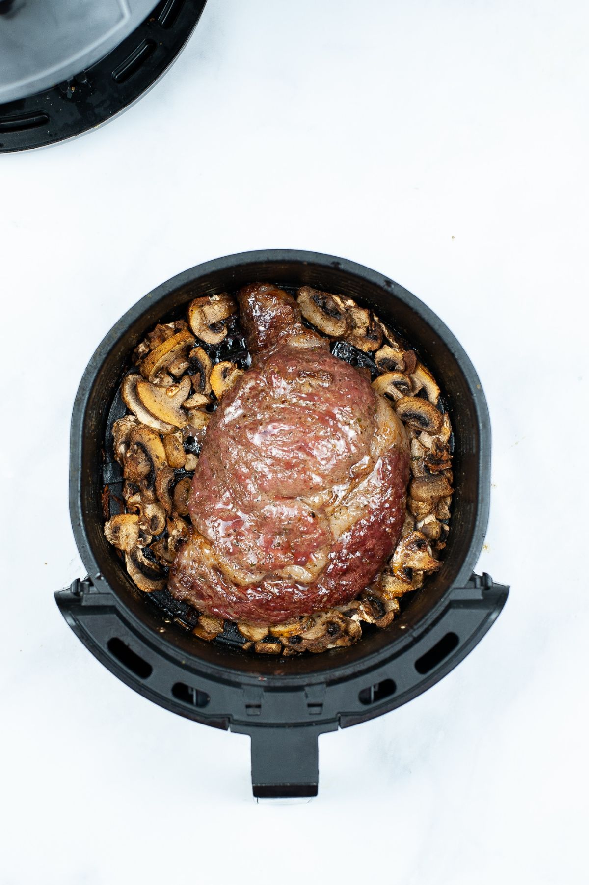 Steak and mushrooms in an air fryer basket.