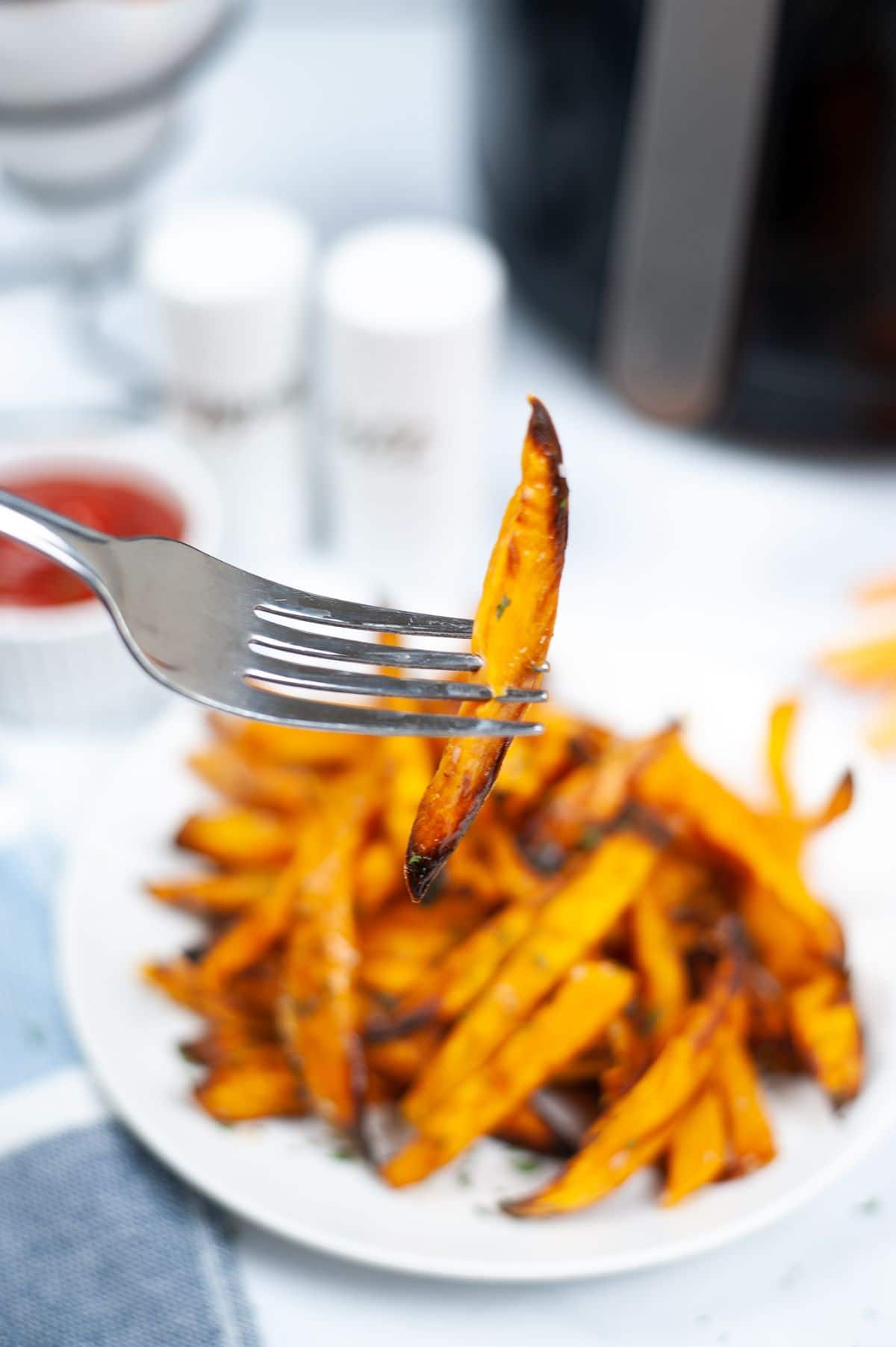 A sliced of Air Fryer Potato Fries picked using a fork, with the rest of the fries blurred at the background.