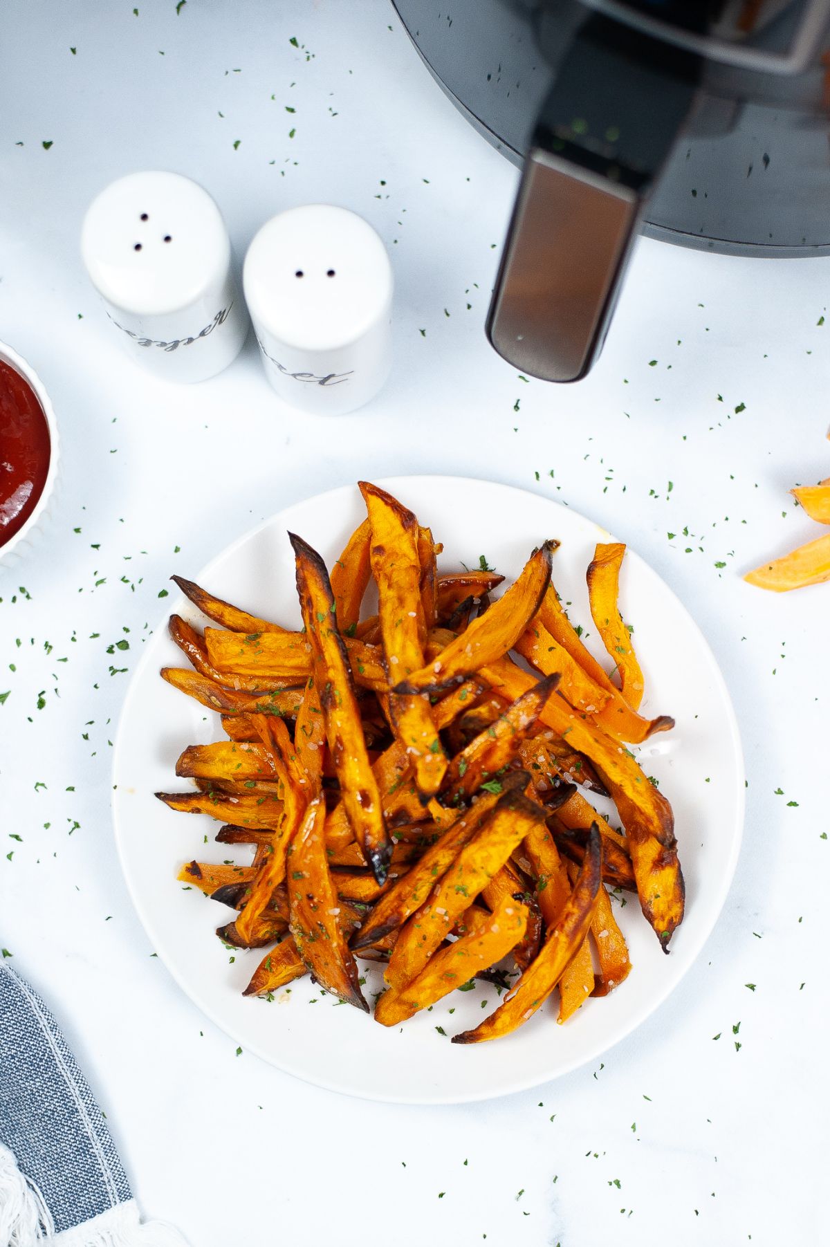An overhead vertical shot of Air Fryer Potato Fries on a white serving plate, with salt and pepper containers and air fryer above it.