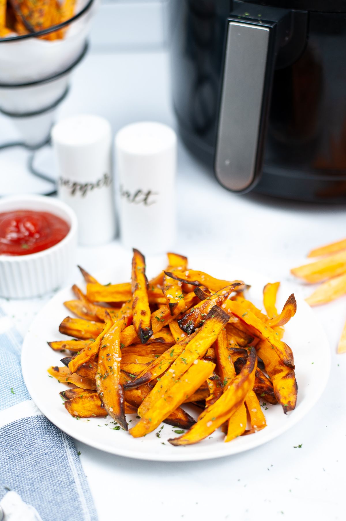 Air Fryer Potato Fries on a white serving plate with a red dipping sauce and air fryer in the background.