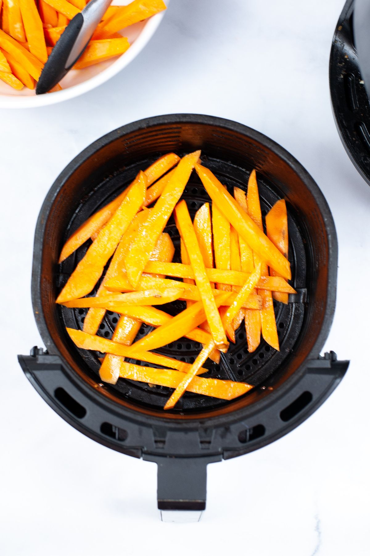Sliced sweet potatoes in an air fryer basket coated with oil.