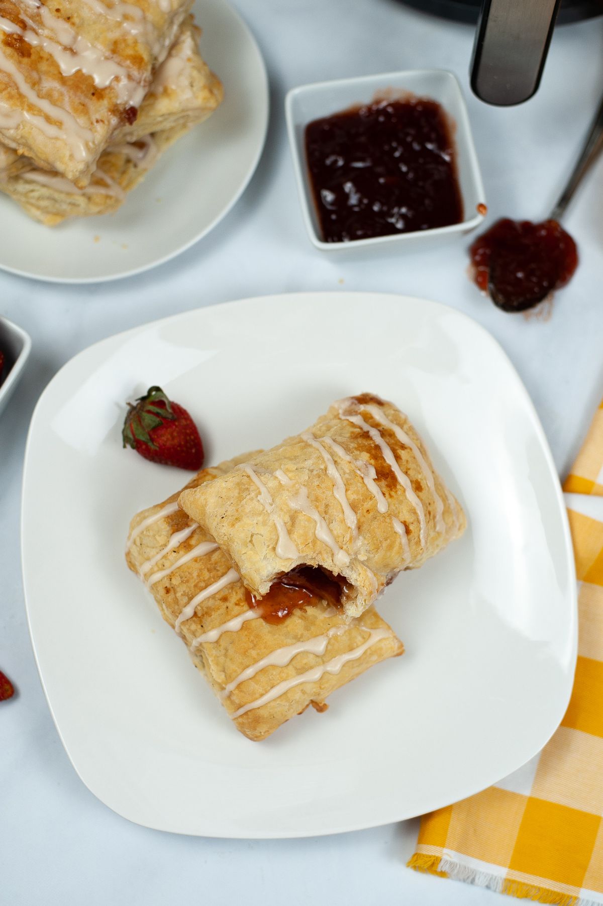 A vertical overhead shot of two pieces of Air Fryer Toaster Strudel on a white serving plate with one of them slightly open to show the strawberry filling.