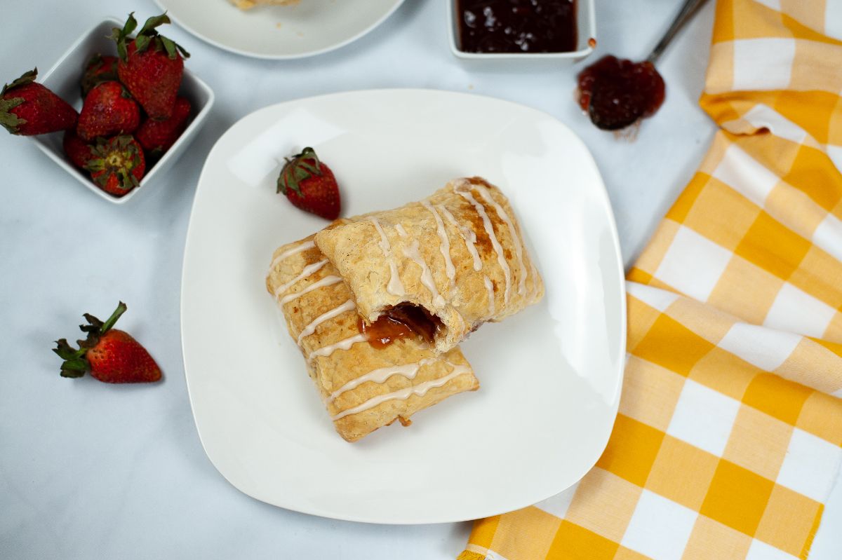Overhead horizontal shot of two pieces of Air Fryer Toaster Strudel on a white serving plate with one of them slightly open to show the strawberry filling.