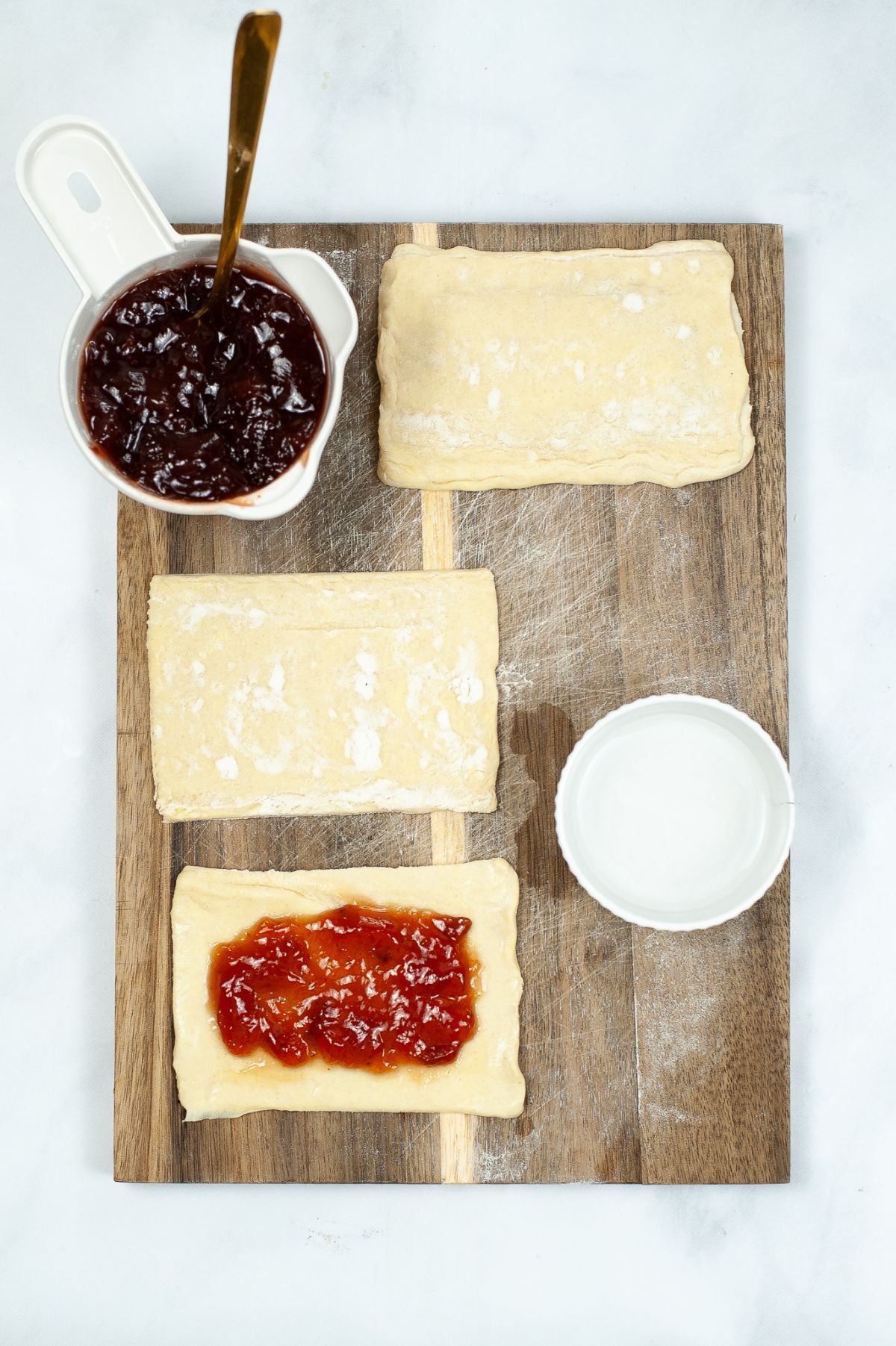 An image of Air Fryer Toaster Strudel being assembled showing a sheet of puff pastry with a jam on top of it and other ingredients around it.