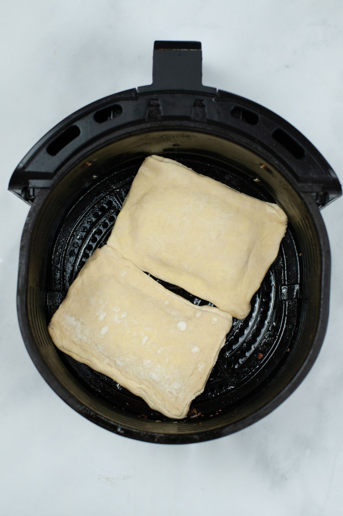 Two assembled puff pastry with jam filling placed in an air fryer basket.
