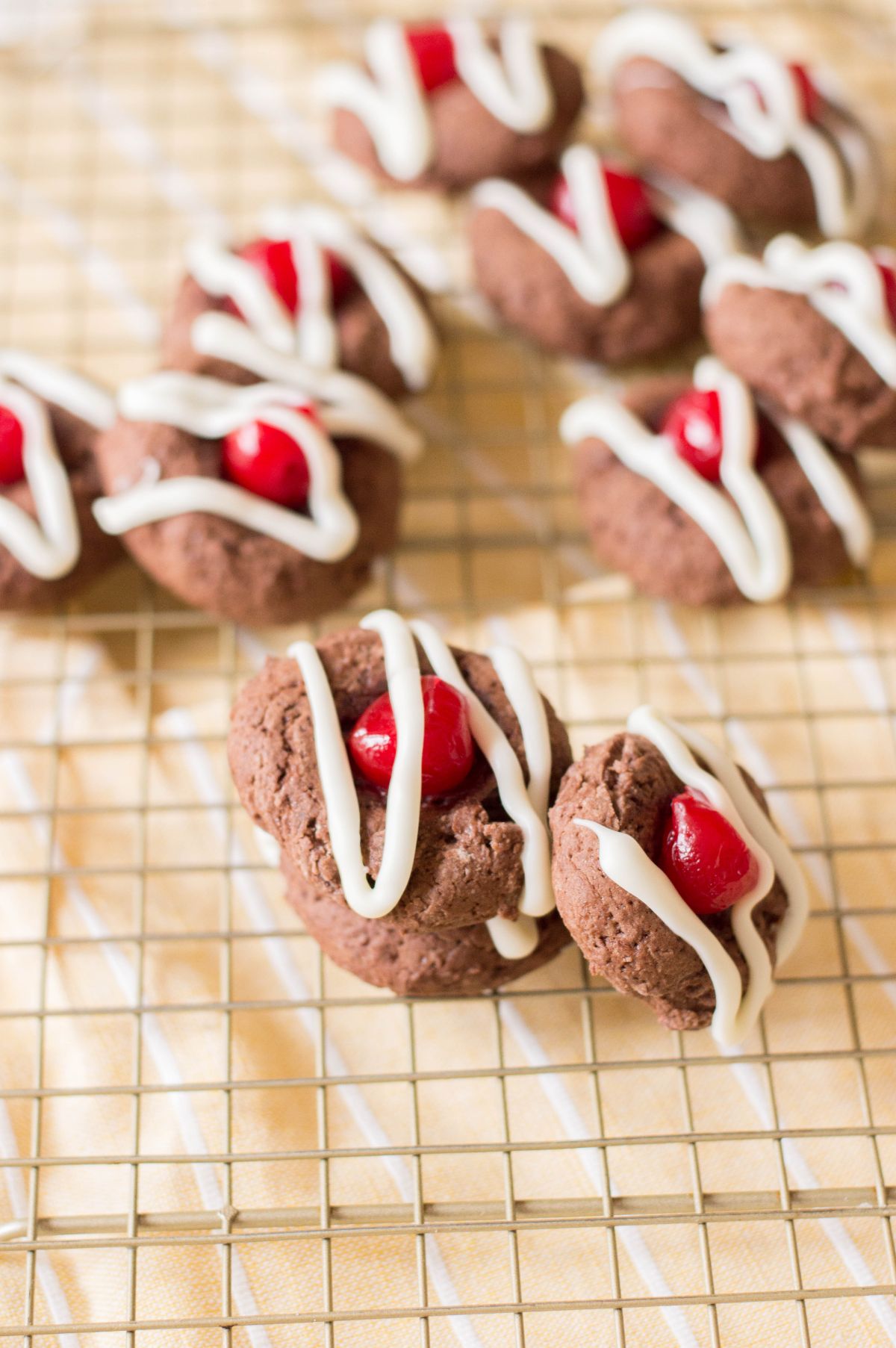 Vertical image of stacked Chocolate Cherry Cookies on a drying rack highlighting two of the cookies.