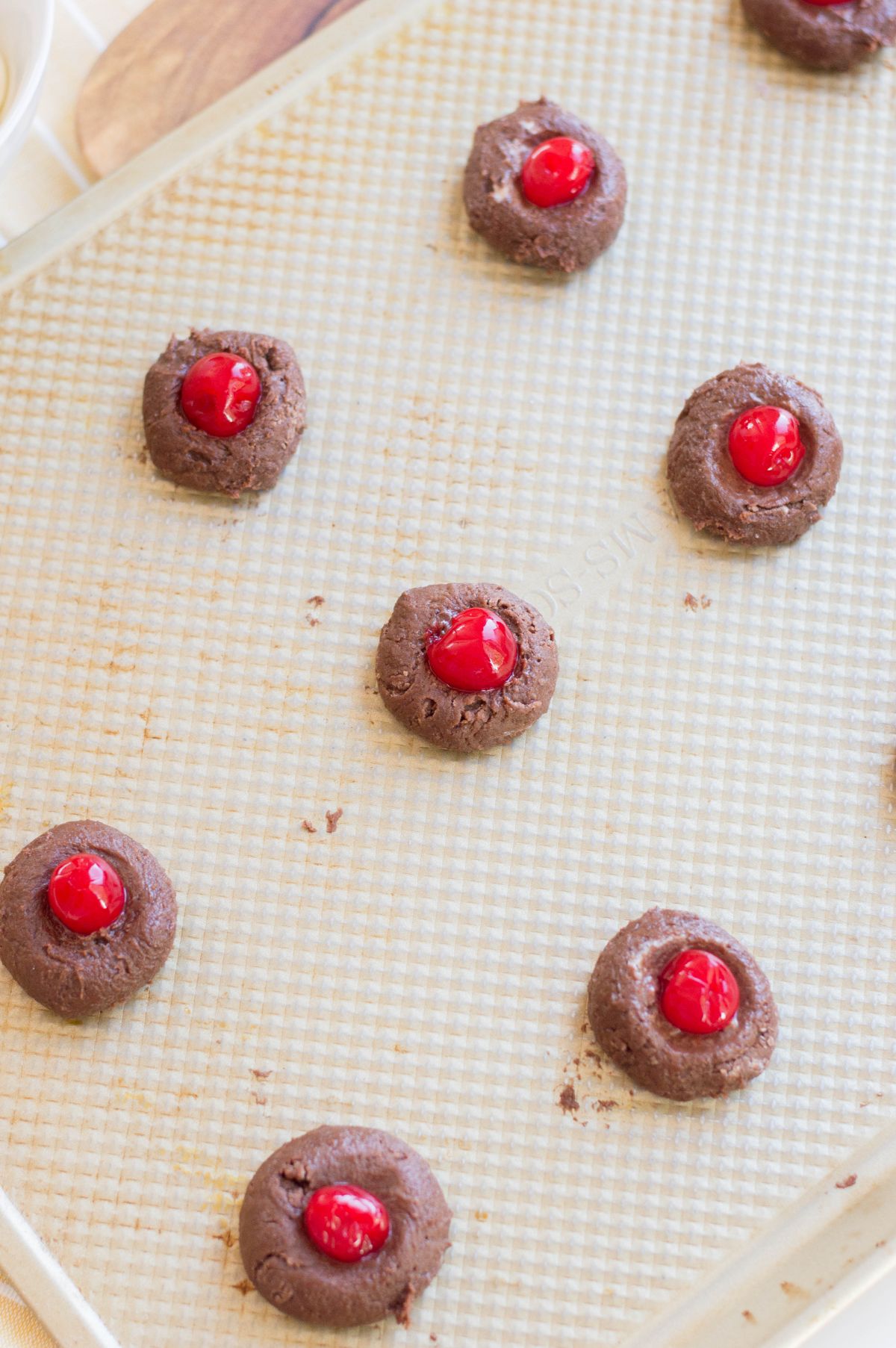 Shaped doung into 1-inch balls with cherry on top of each of them, placed on a baking sheet.