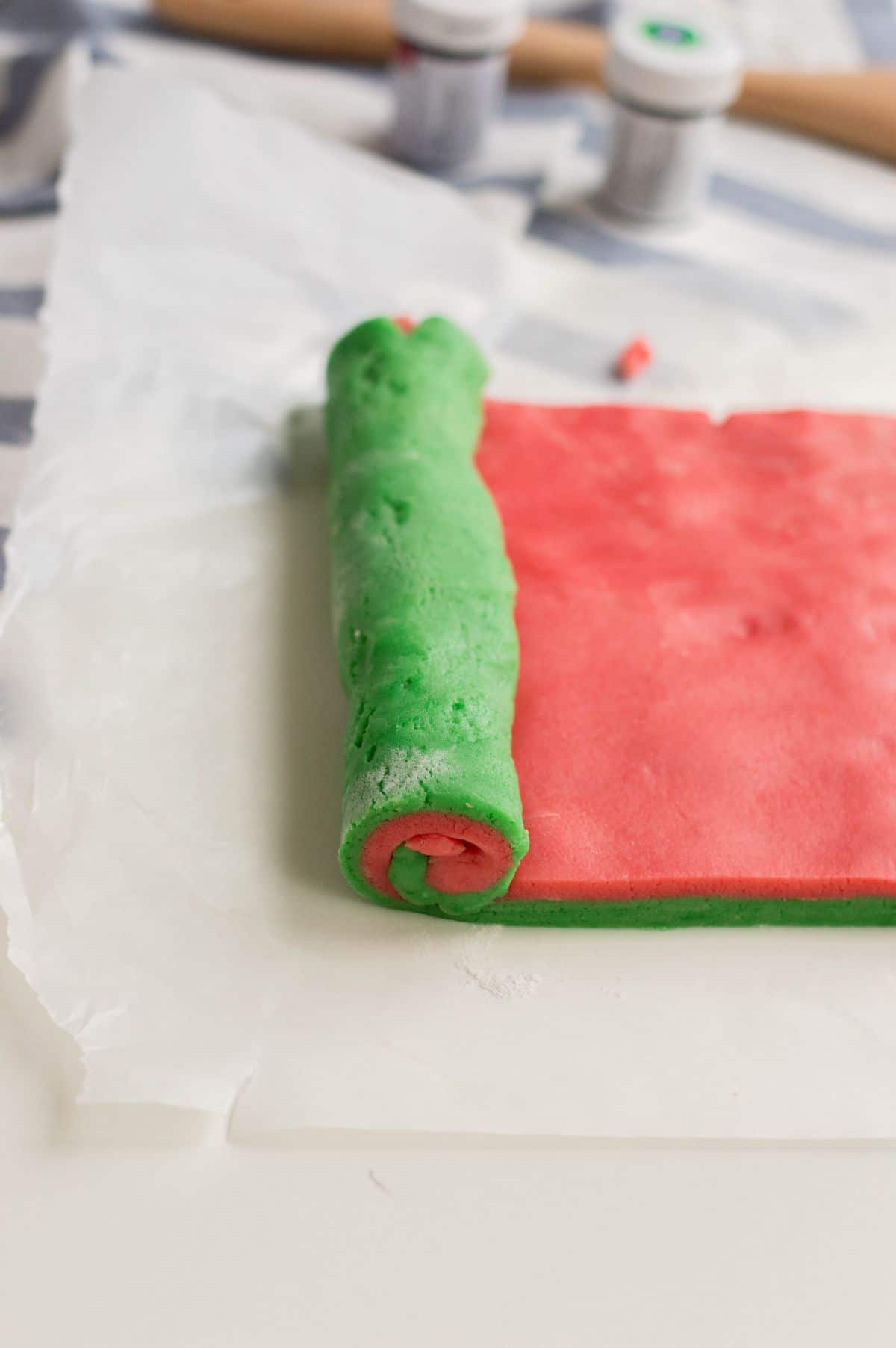 Stacked red and green rectangular flattened dough and being rolled to form a pinwheel cookie log.