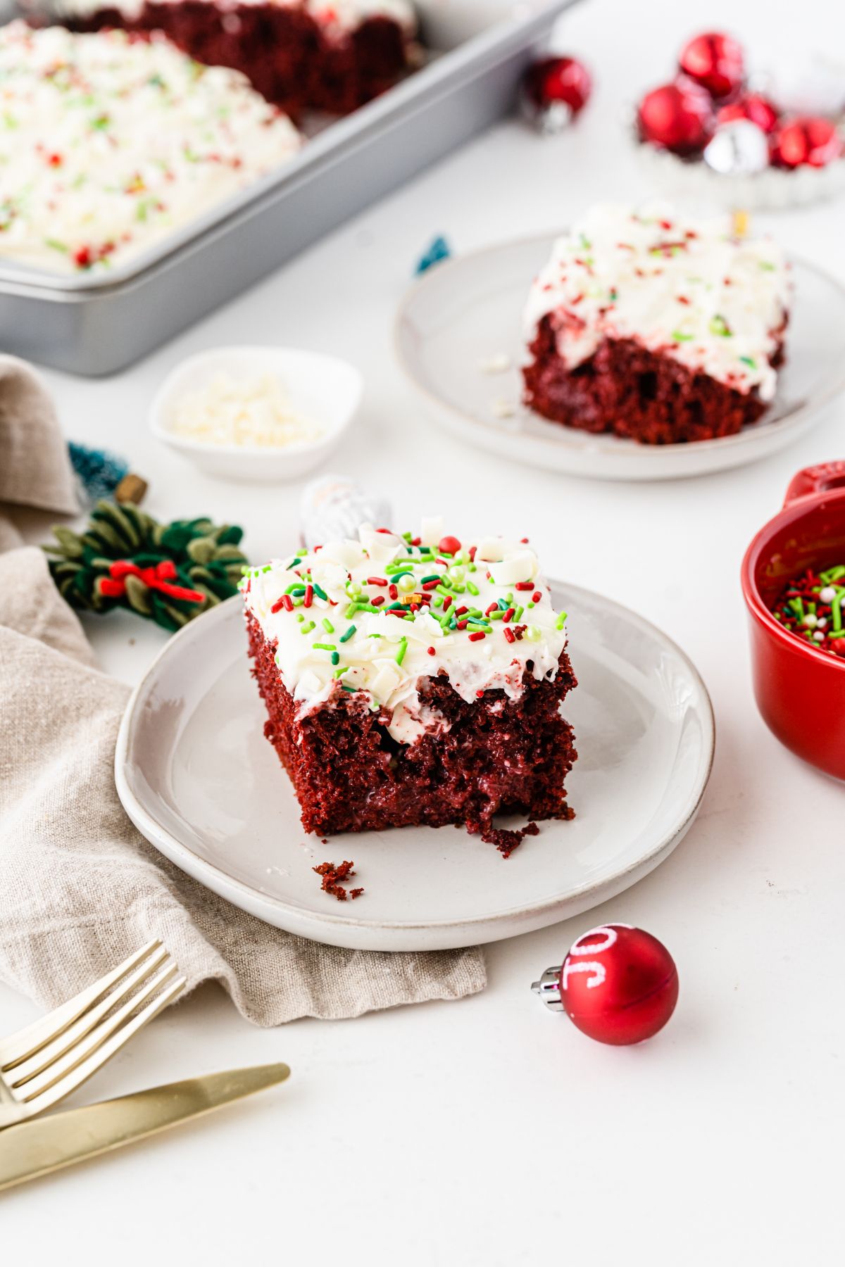A square slice of Christmas Poke Cake on a small white serving plate with more cake in the background.