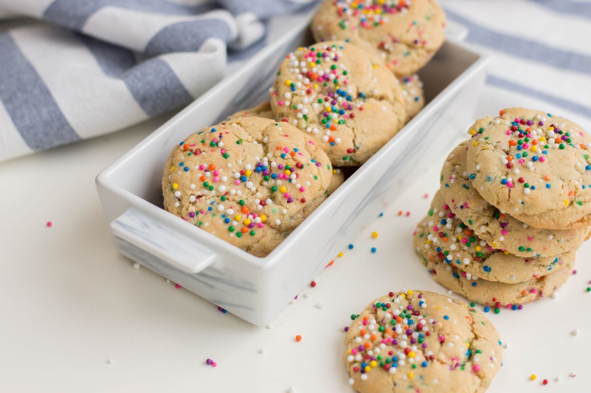 A horizontal image of Funfetti cookies,  in a rectangular ceramic serving dish, with a stack of 4 cookies beside it and a single cookie in front of the stack.