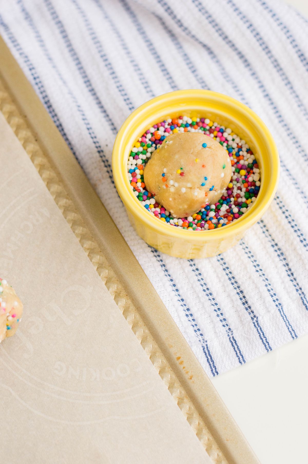 A shaped cookie dough being rolled in a bowl of sprinkles.