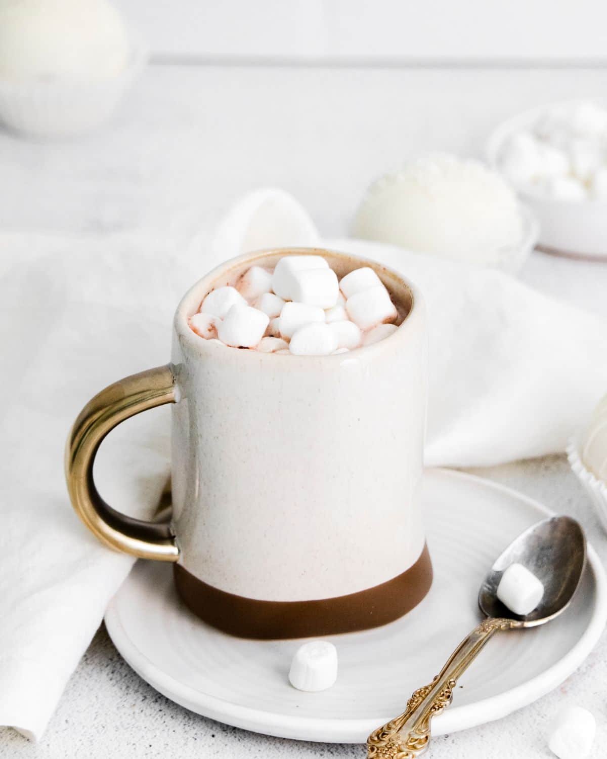 A mug of White Chocolate Hot Cocoa Bomb with milk in it and marshmallow toppings.
