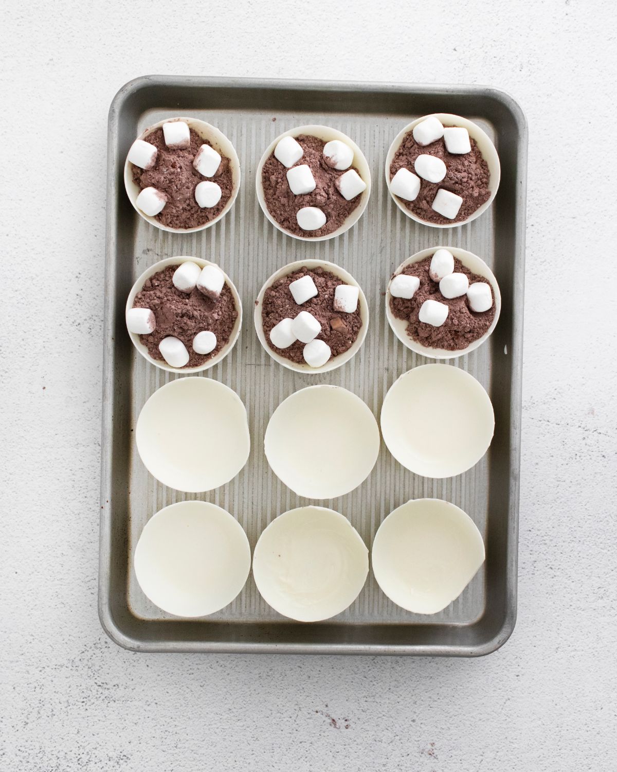 White chocolate molds in baking pan, half of it have cocoa mix and few mini marshmallows.