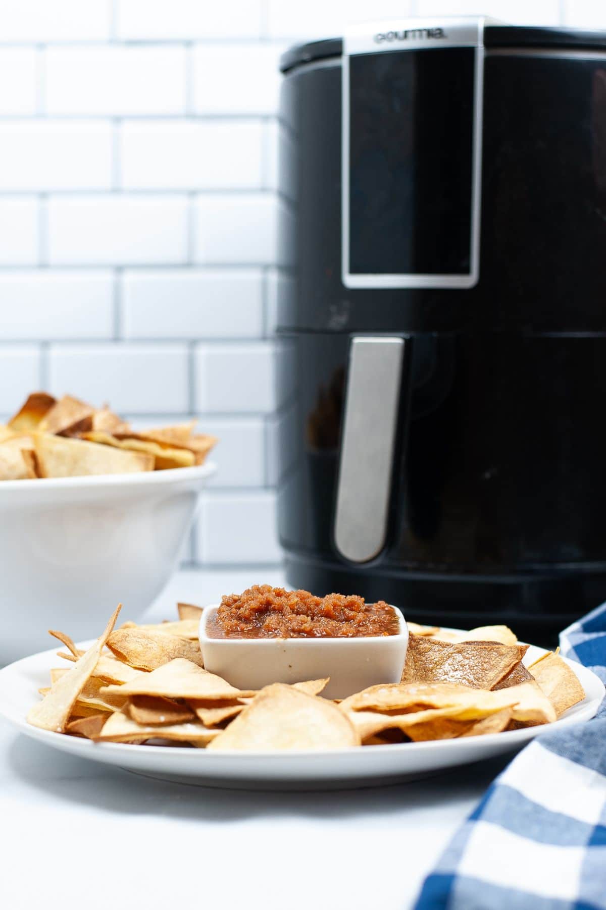 Air Fryer Tortilla Chips on a white serving plate with the air fryer in the background.