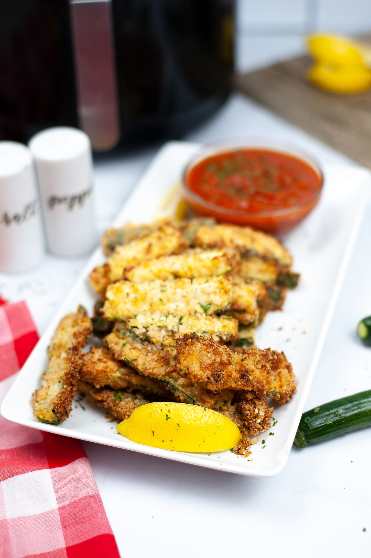 A batch of Air Fryer Zucchini Fries on a white serving plate with a red sauce at the end of the plate.