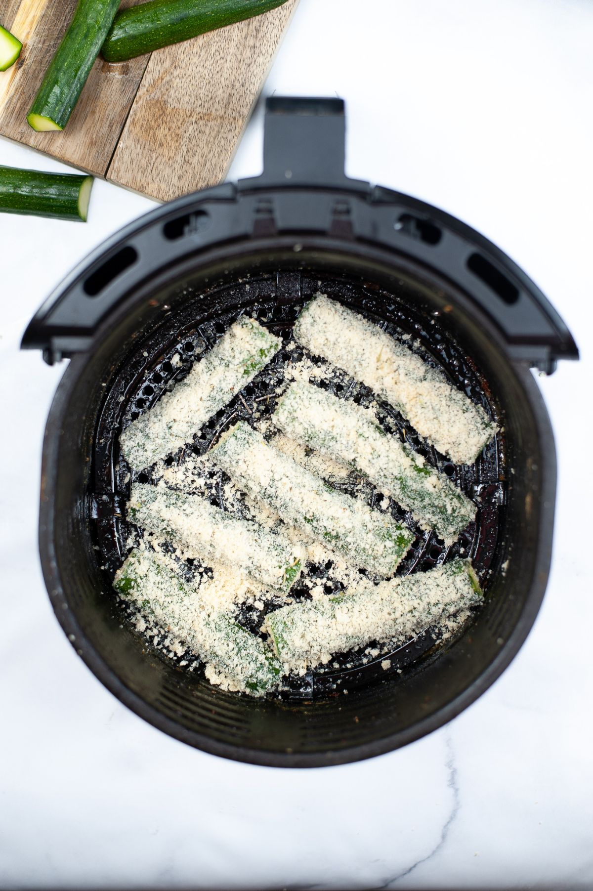 Coated Zucchinis in an air fryer basket.