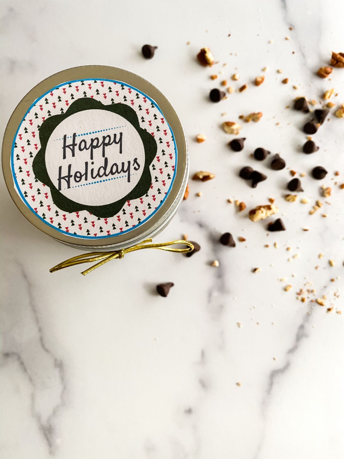 Overhead shot of the Brownie Mix in a jar showing the text at the top of the jar saying "Happy Holidays" next to chocolate chips on a counter