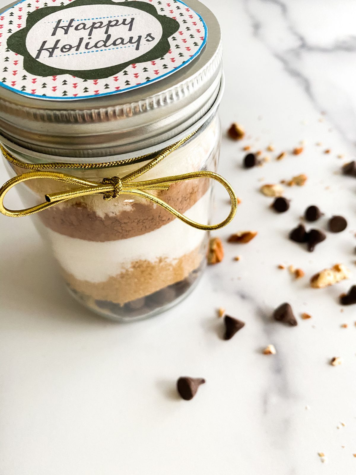 An angled shot of the Brownie Mix in a Jar showing a part of the text on top of the jar cover which reads Happy Holidays, and the side of the jar which showcases its layers of the brownie mix.